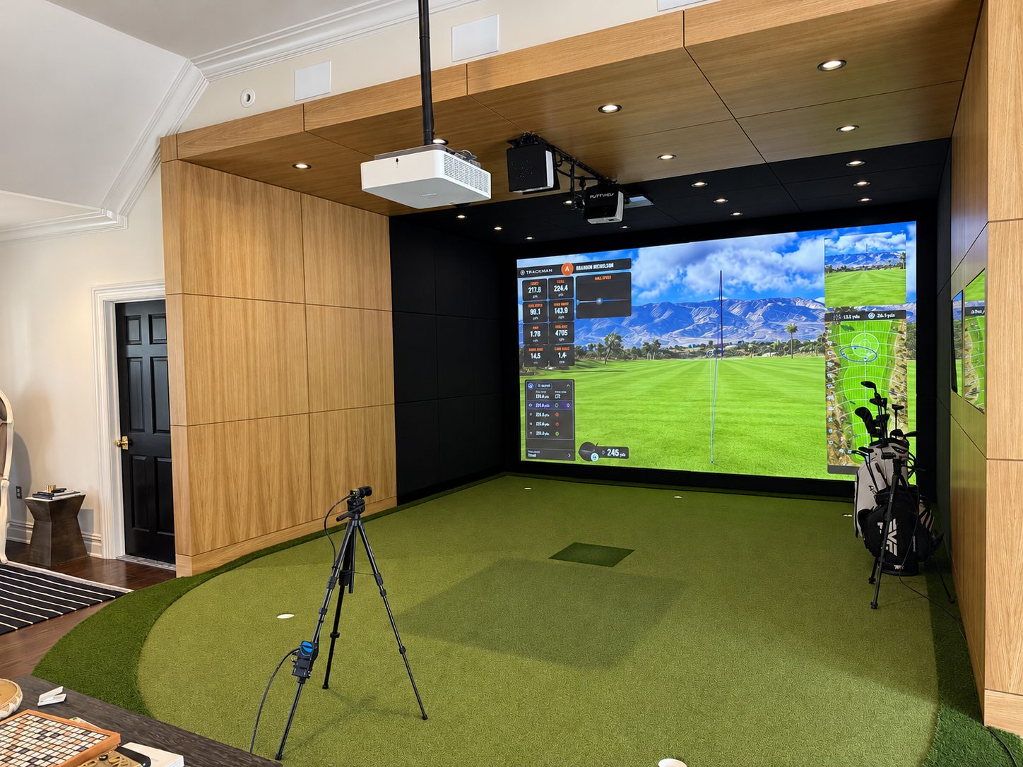 Angled view of the wood-paneled simulator enclosure, projector and turf hitting area