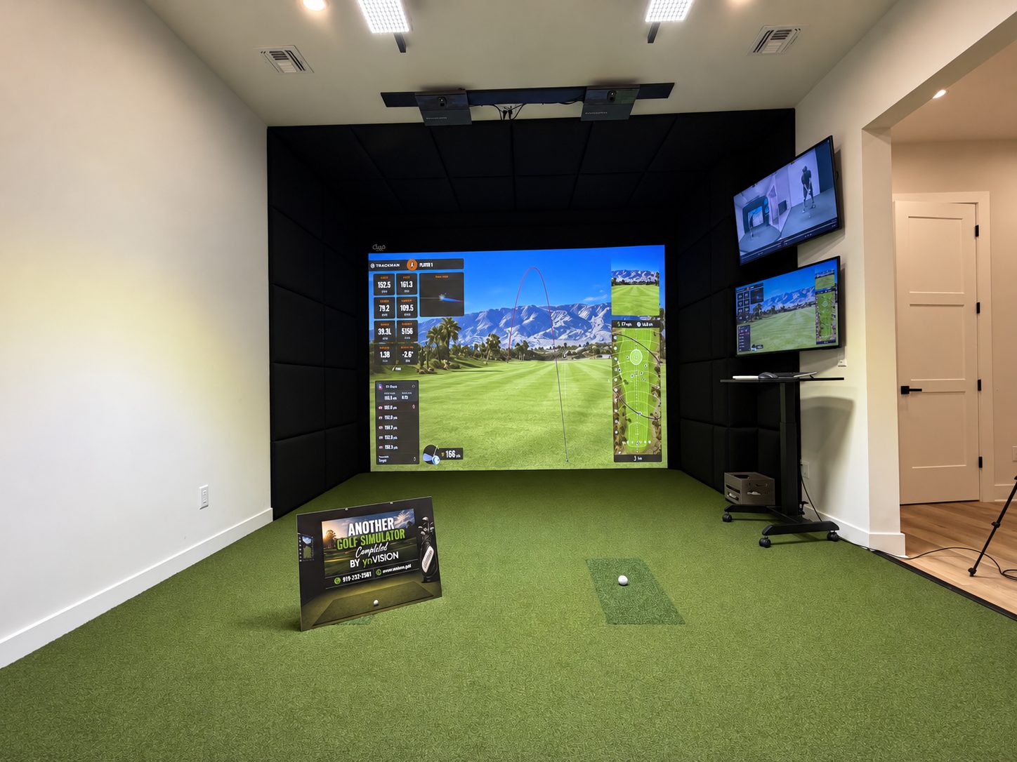 Wide view of a TrackMan simulator room with two overhead units and a projected course