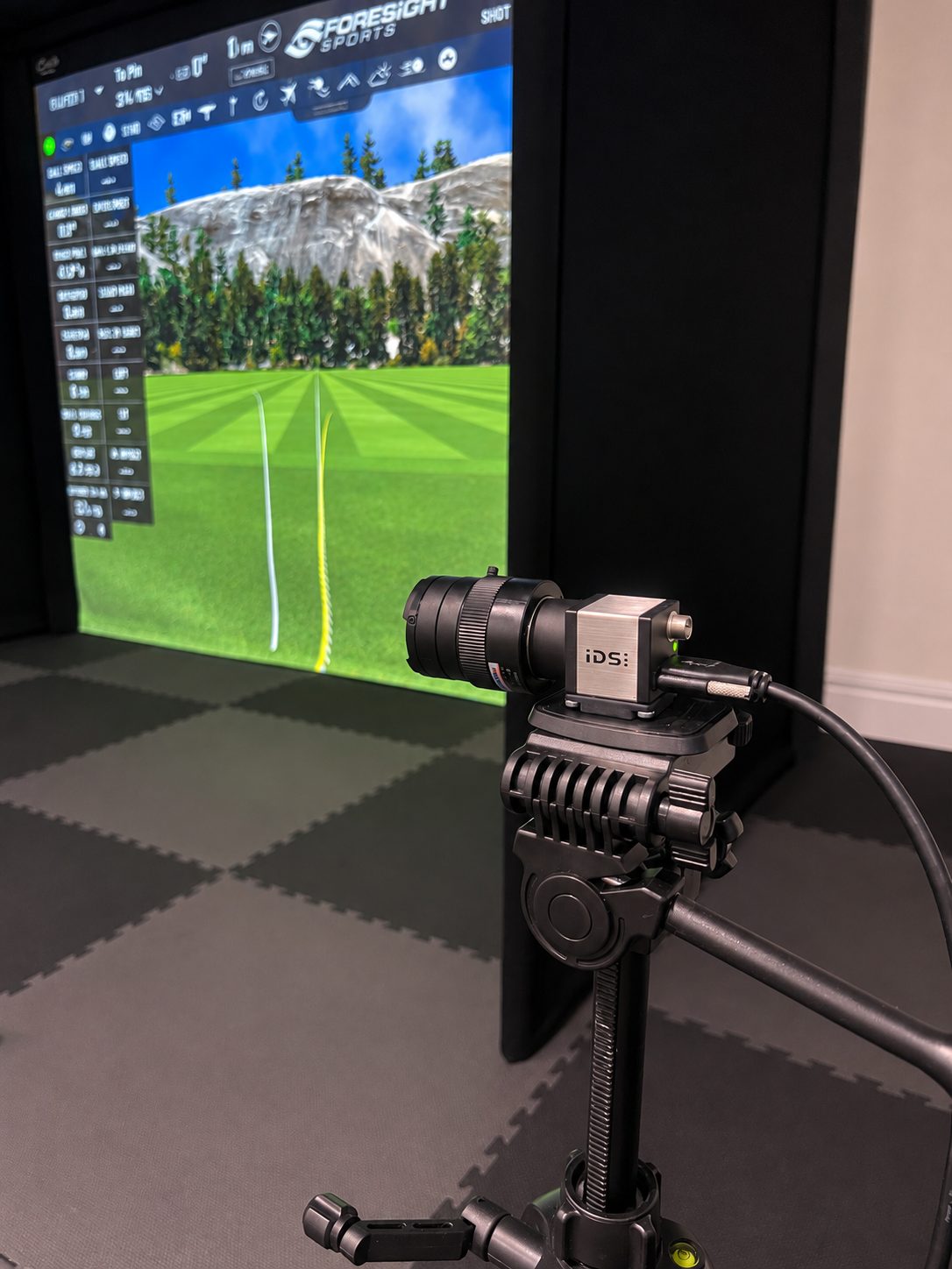 Close view of a swing-analysis camera beside a Foresight simulator screen