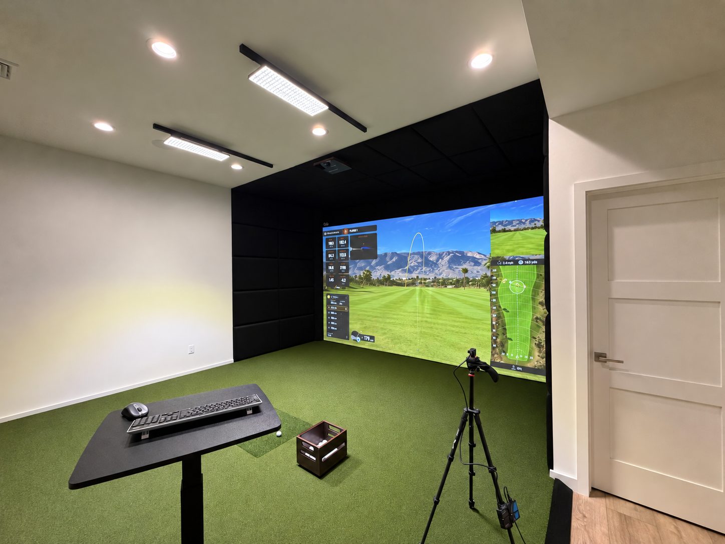 Angled view of a finished TrackMan simulator room with padded walls and turf